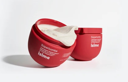 Imagem de dois potes vermelhos arredondados do produto capilar da Shakira, a Máscara Tripla Reparadora Isima, sendo um deles aberto e exibindo a textura cremosa e consistente da fórmula. O design moderno das embalagens em tom vibrante transmite inovação e energia, reforçando a proposta de tratamento intenso para os fios.